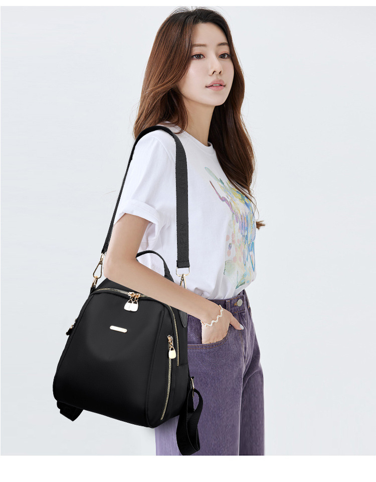 Elegant black SKUGG women’s mini backpack handbag with gold zippers and adjustable shoulder strap, displayed on a beige studio background.