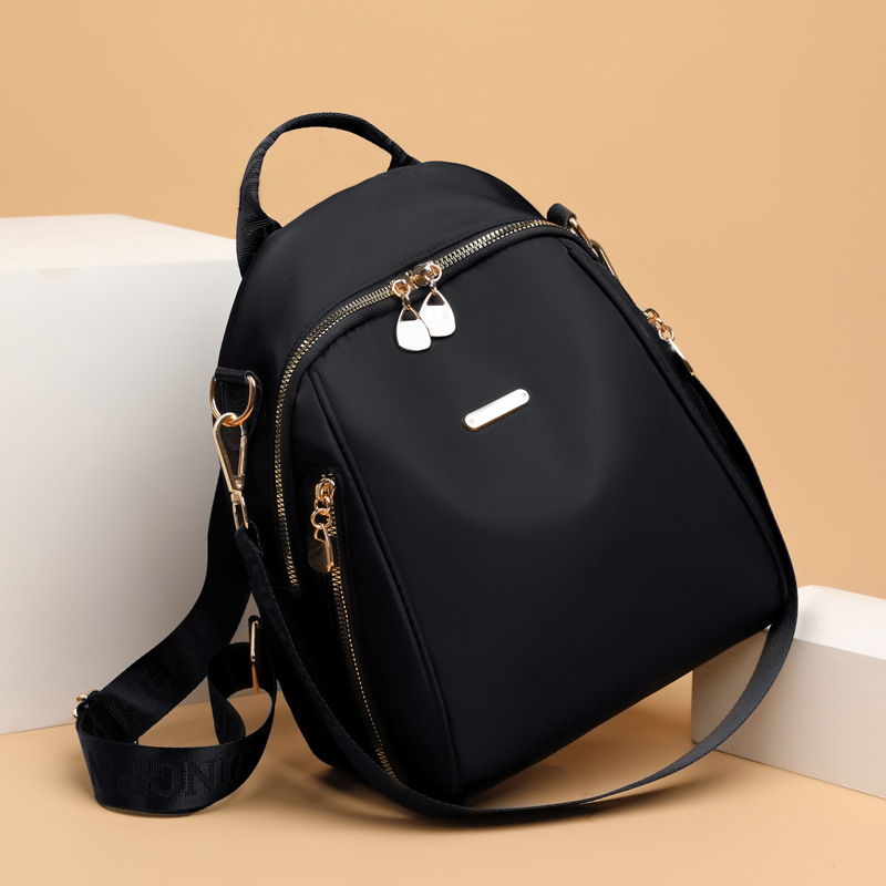 Elegant black SKUGG women’s mini backpack handbag with gold zippers and adjustable shoulder strap, displayed on a beige studio background.